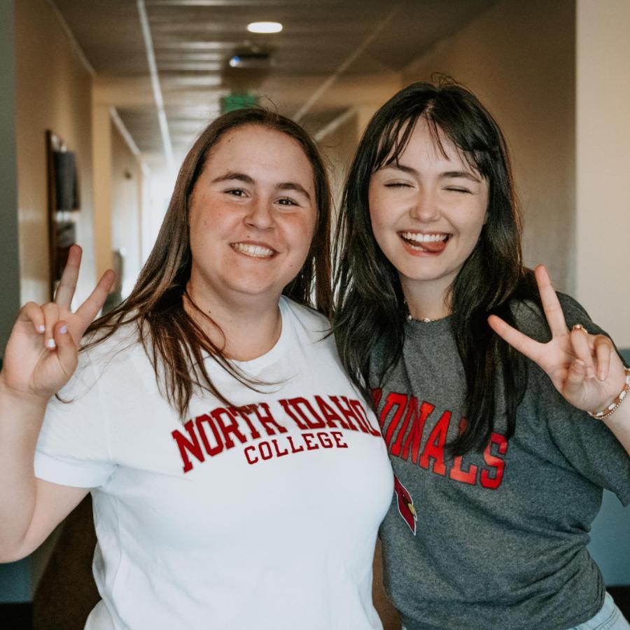 900x900 2 female students in resident hall making silly faces giving peace signs with their hands