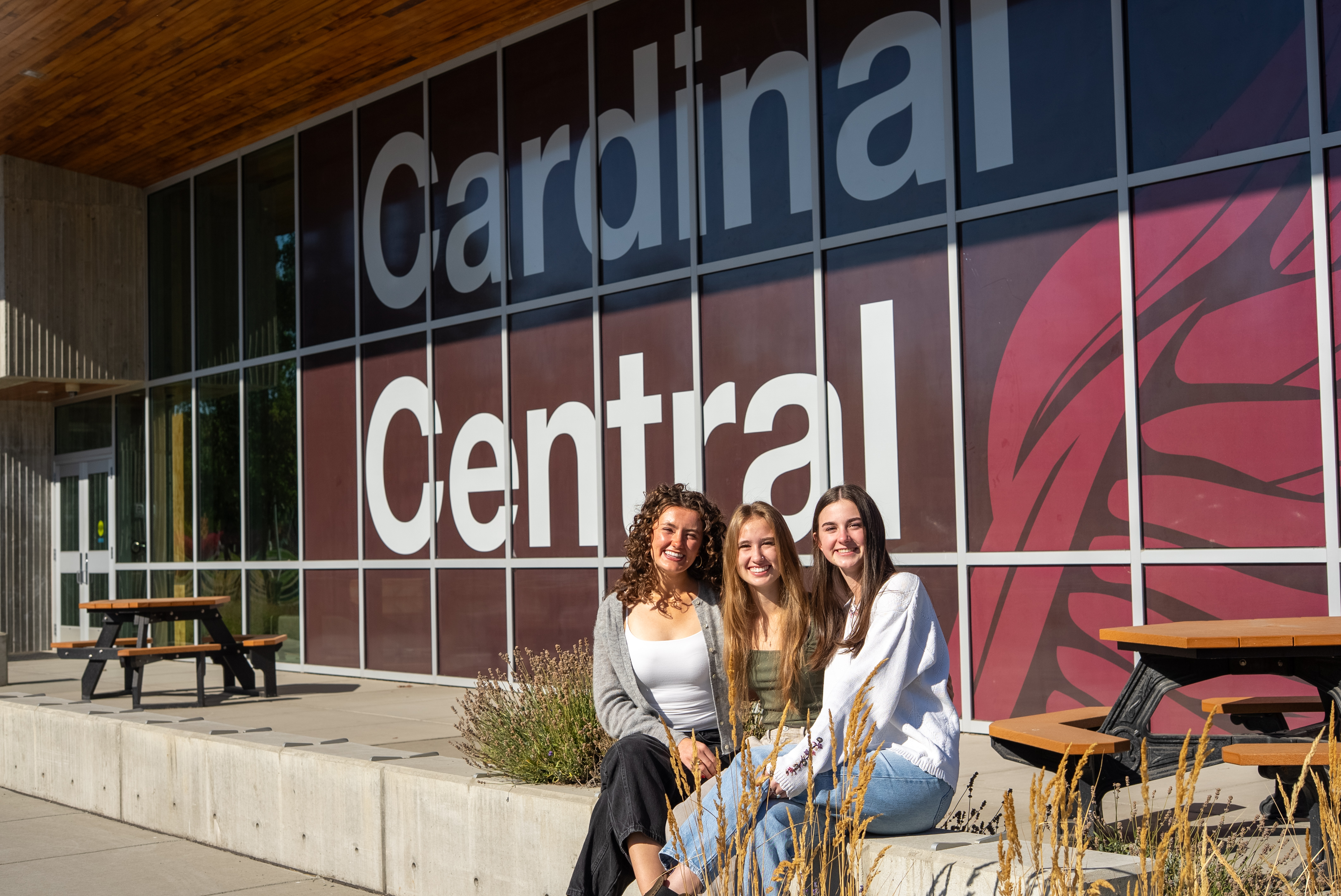 cardinal central side building outside, with 3 female student sitting