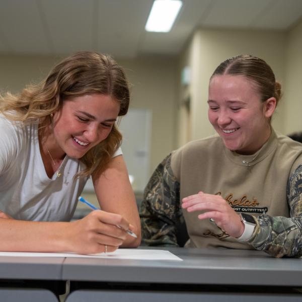 2 female students smiling at table together
